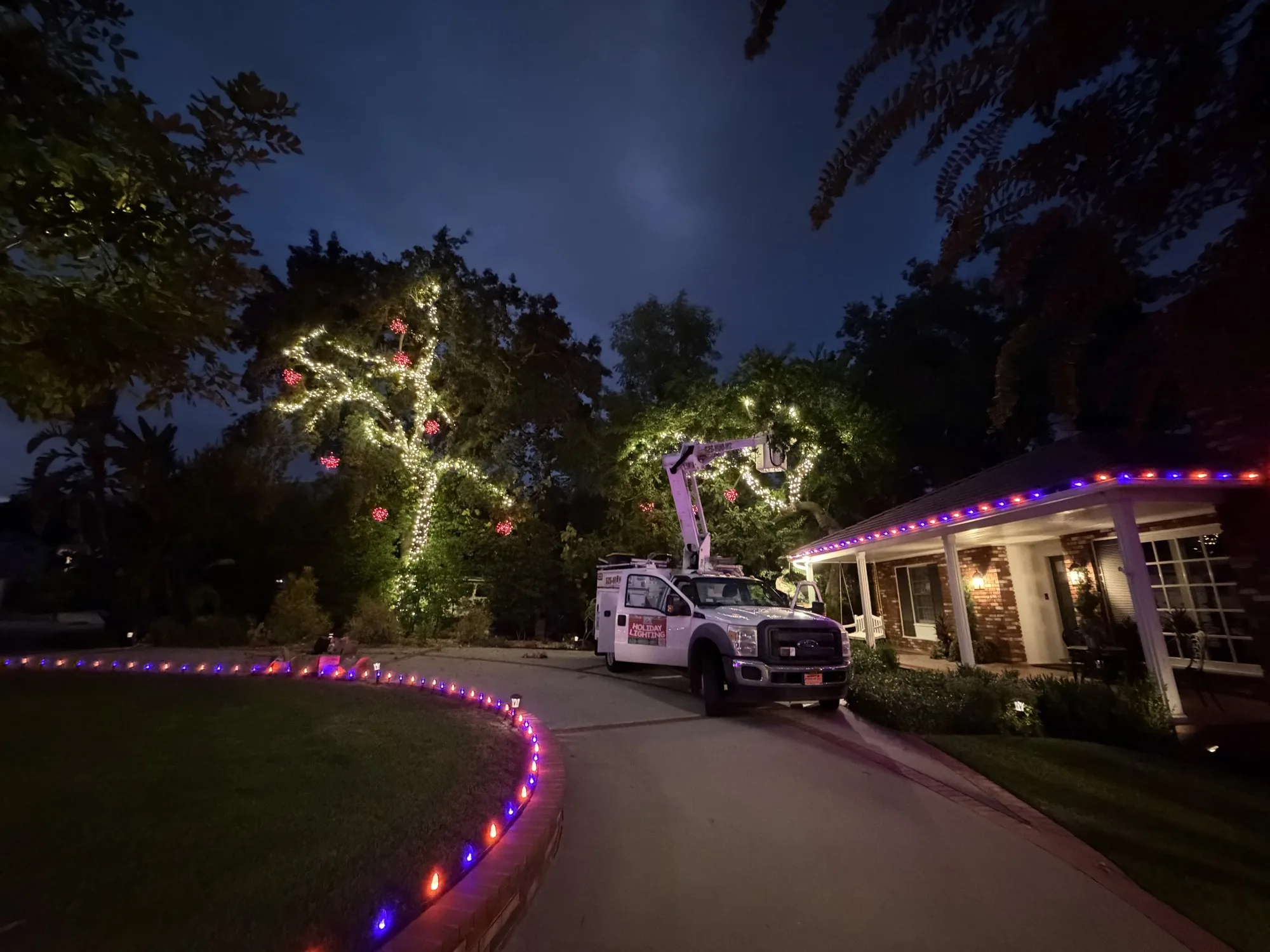 Bee Merry bucket truck on-site installing roofline lights and a wrapped tree
